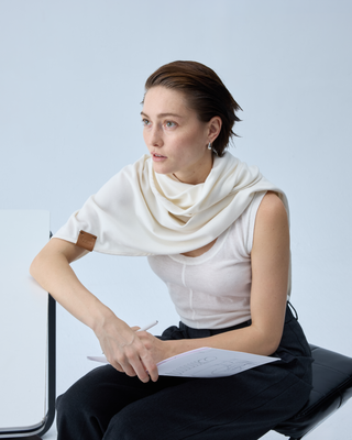 Woman seated at a desk wearing a white wool wrap and holding fashion sketches