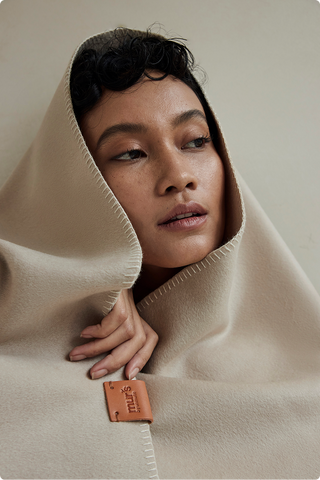 Close-up of a model wrapped in a cream wool blanket with contrast stitching