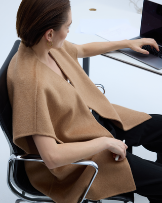 Woman wearing a camel wool cape while working on a laptop