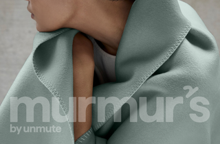 Person wearing a light green blanket with 'murmur's by unmute' branding.