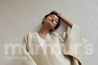 Person wearing a beige sweater over a white shirt against a plain background