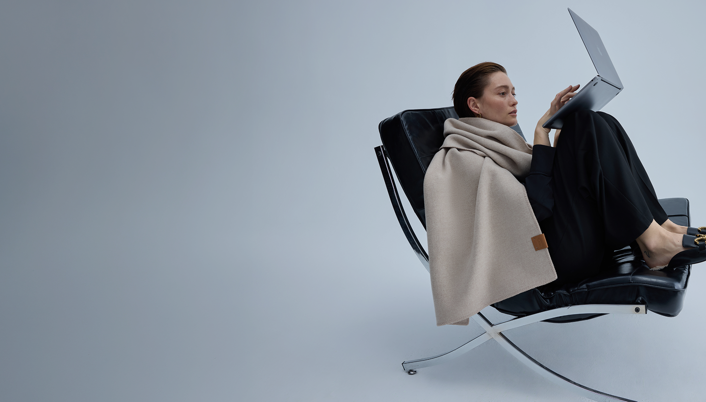 A woman wrapped in a Murmurs throw, working from a lounge chair