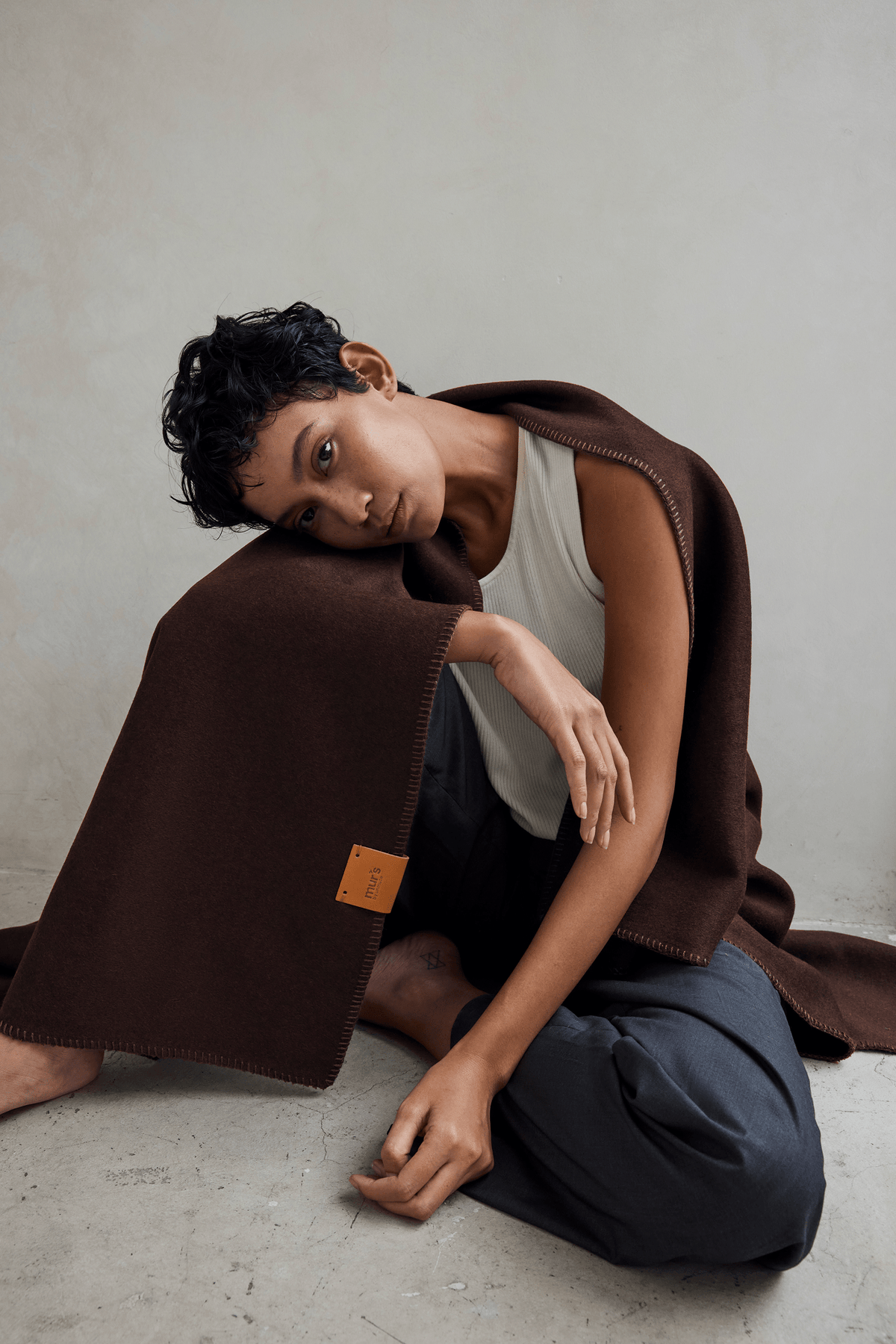Woman seated, wrapped in the Hush 100% wool throw blanket in Cinnamon Bark rust brown
