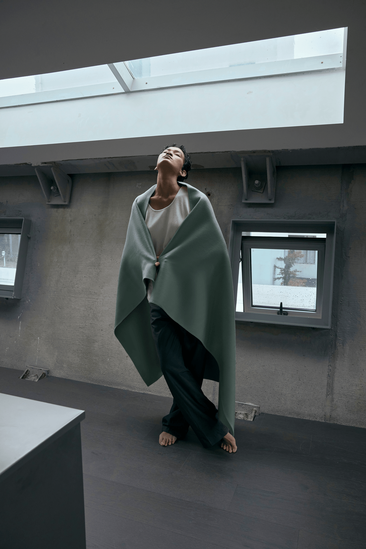 Woman standing by a window with the Lilt mint green wool blanket in Mist Mint over her shoulders