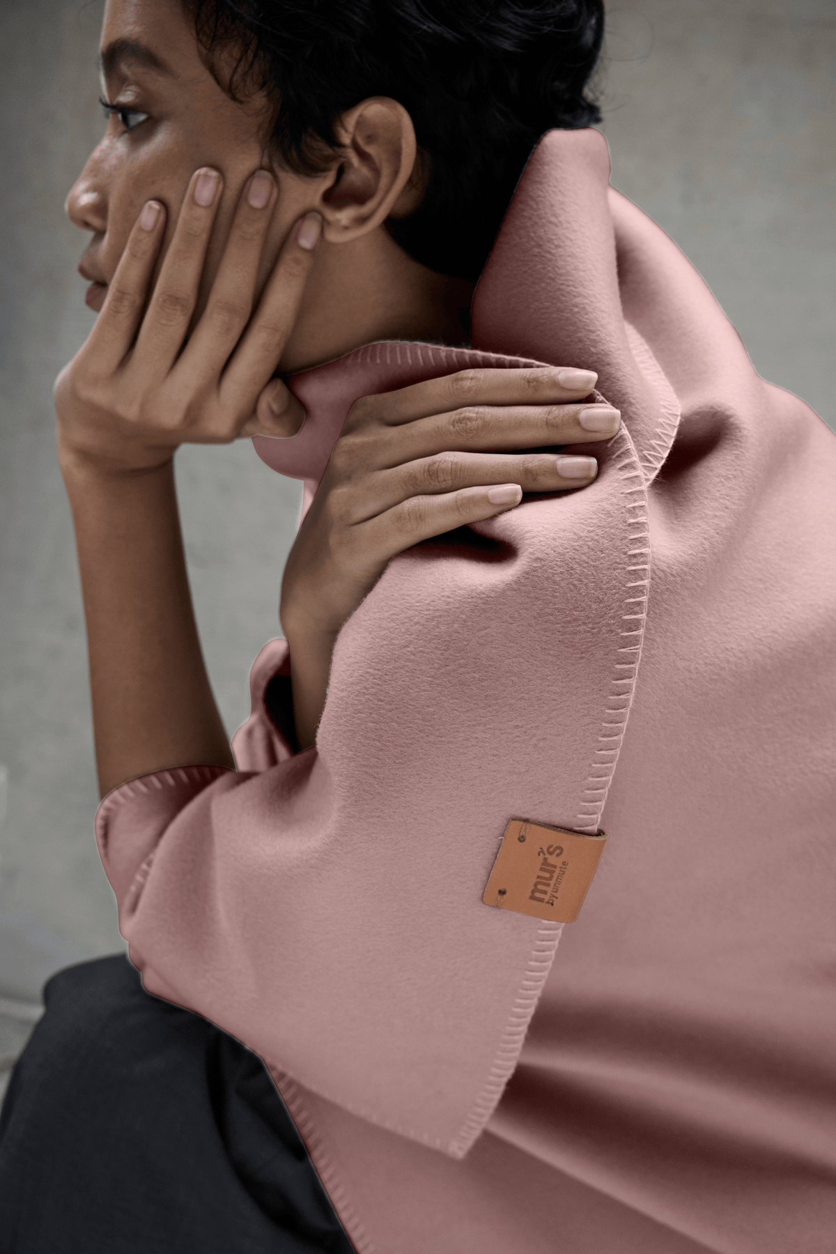 Woman seated with the Lilt lambswool and cashmere blanket in Sunsoft Peach across her lap