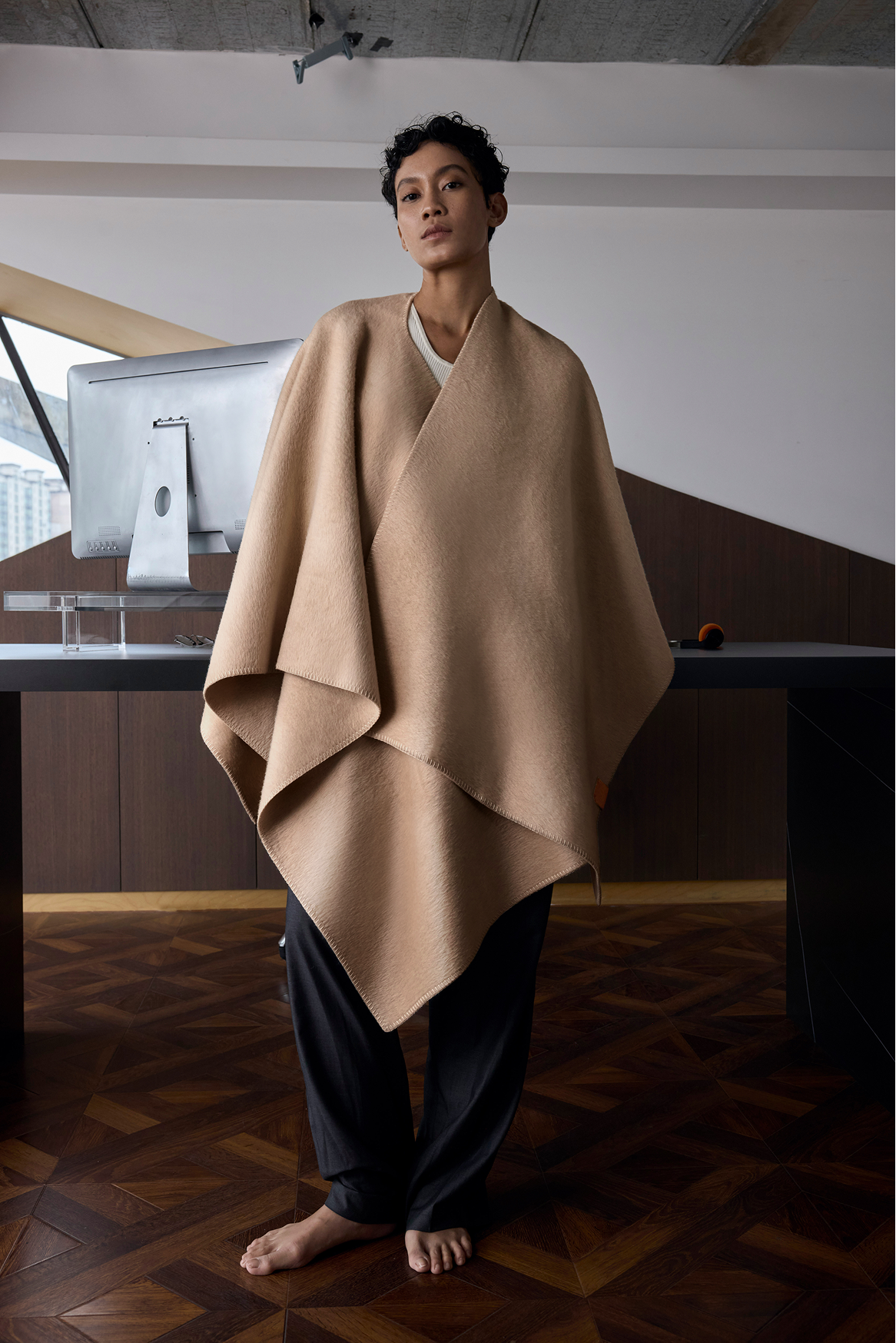 Woman standing in a wood-floored room wearing the Murmur camel hair ruana in Cedar Dust at full length