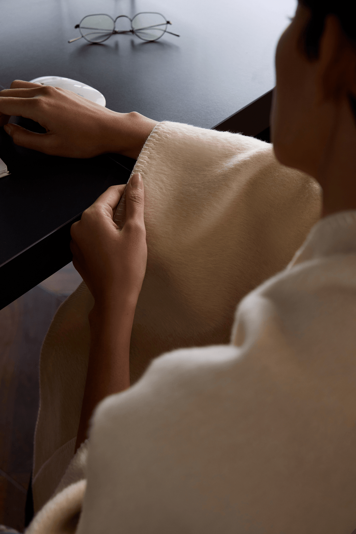 Woman at a table folding the Veil camel hair blanket in Sand Dune, small enough for a carry-on